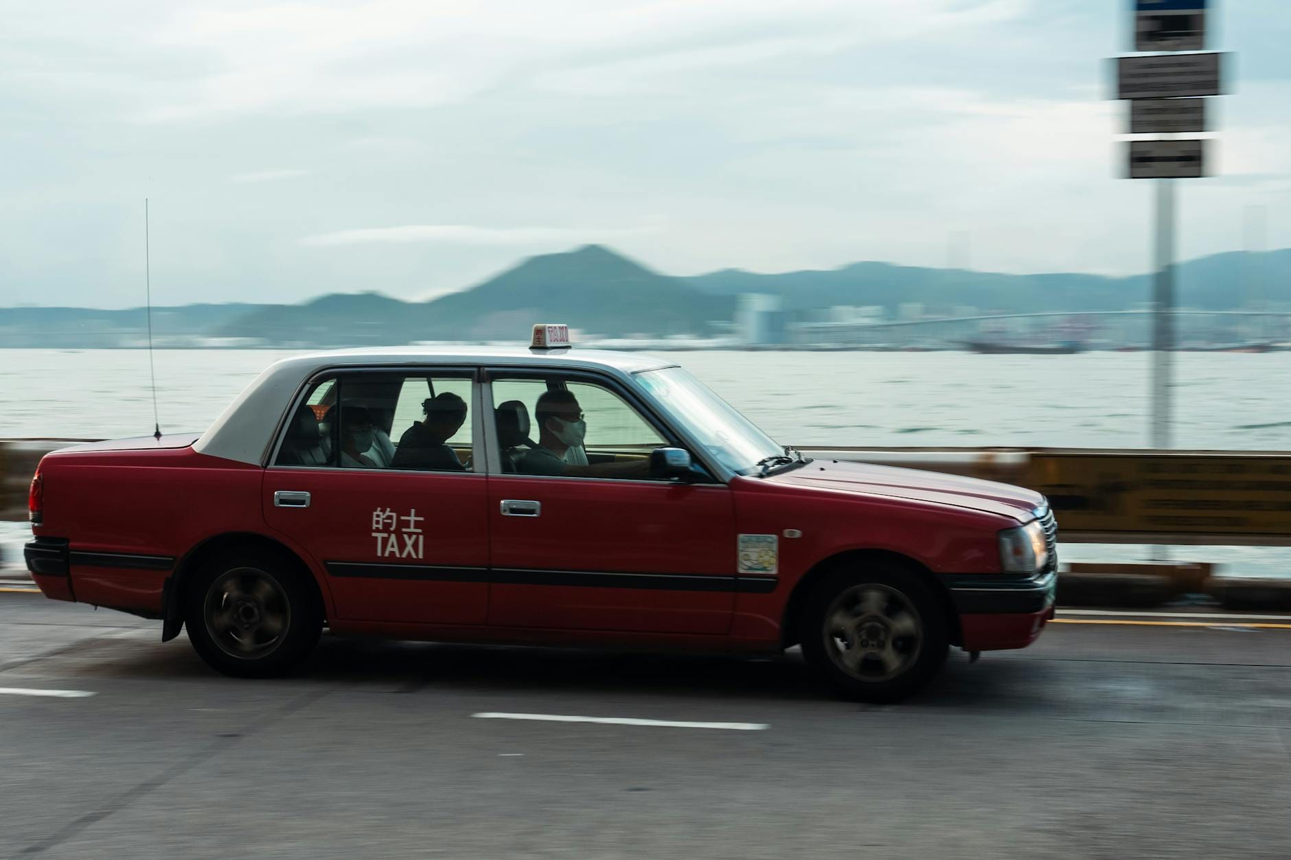 Czerwony taksówka jedzie nadmorską drogą z górami w tle