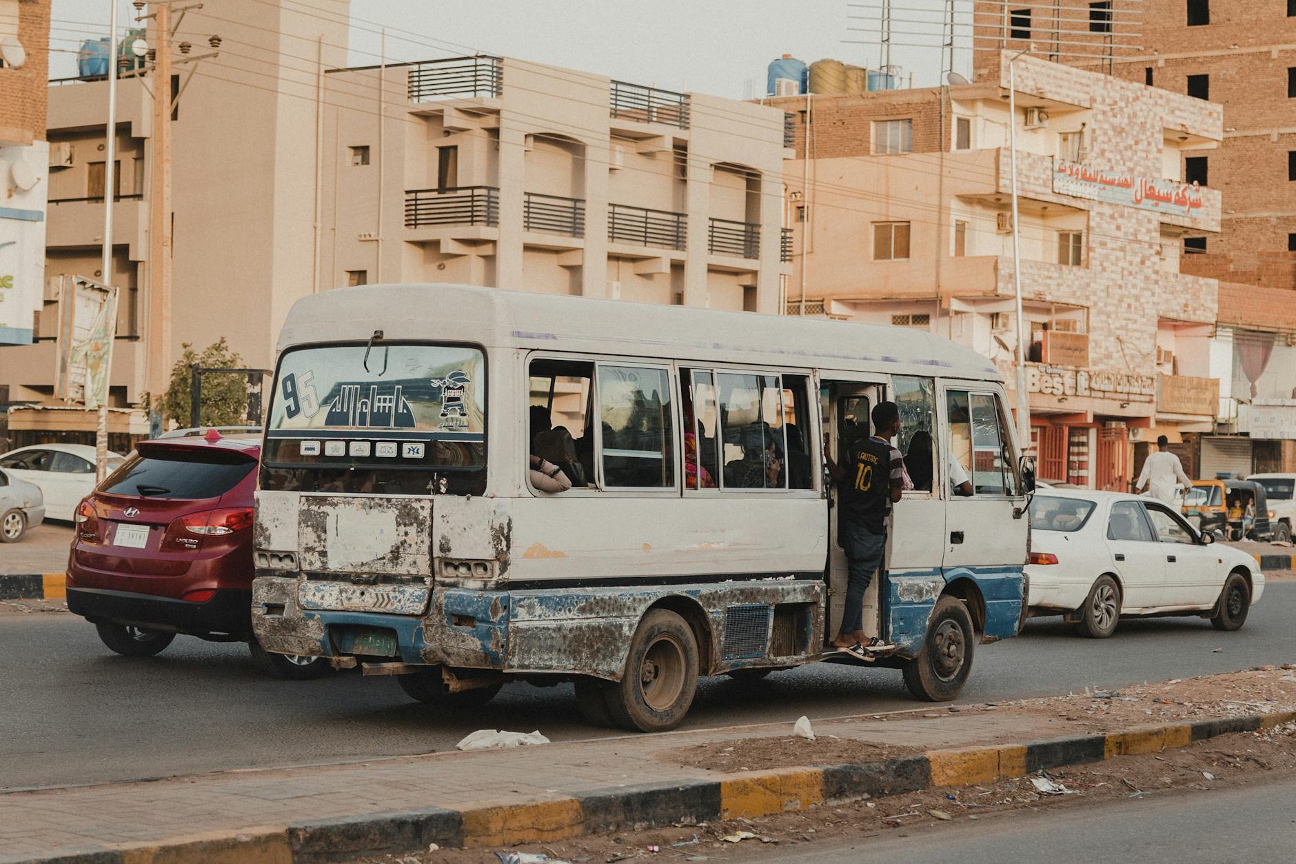 Biały minibus jedzie ruchliwą ulicą w centrum dużego miasta