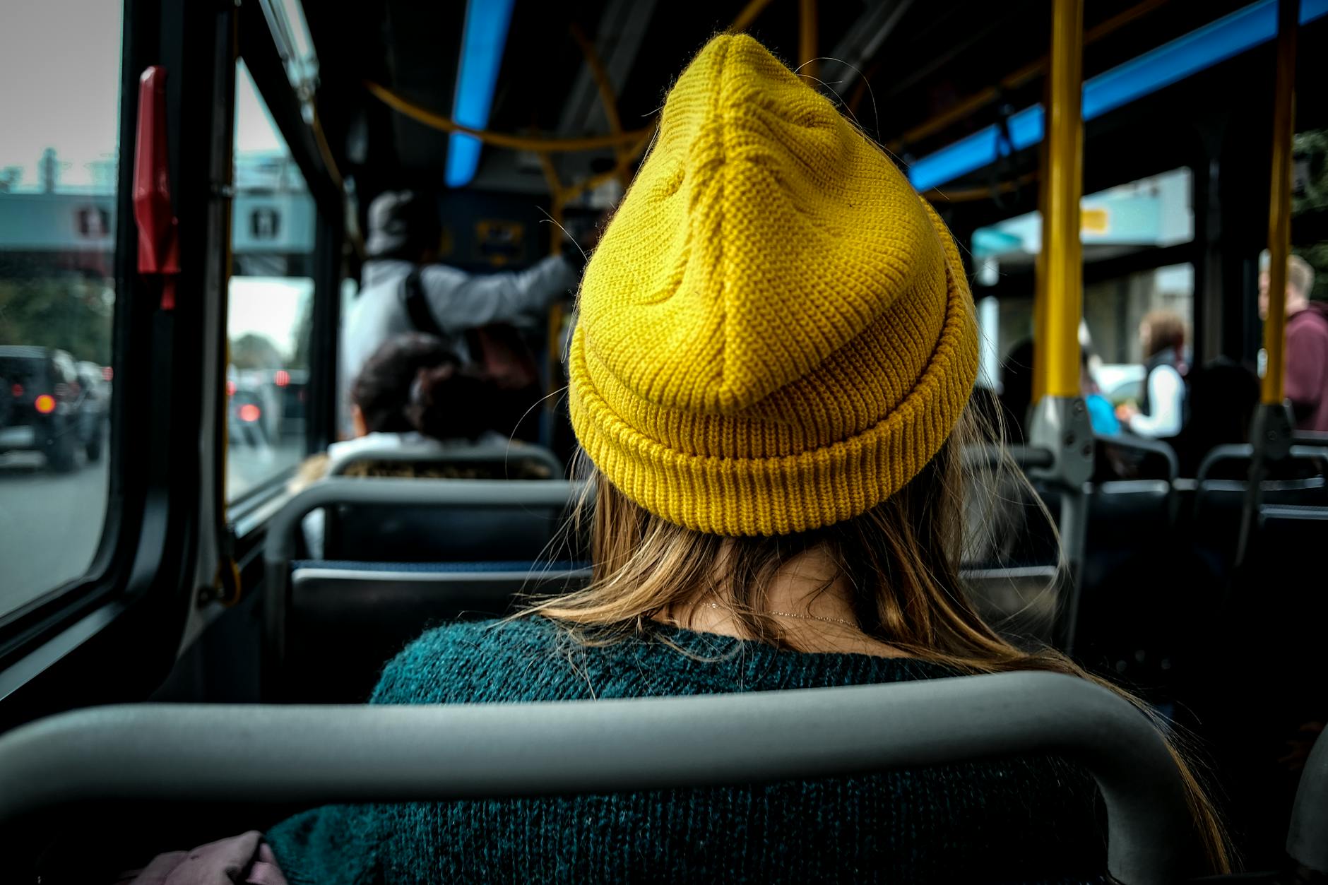 Kobieta w żółtej czapce jedzie miejskim autobusem, widok z tyłu