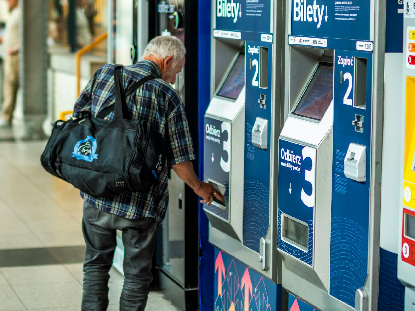 Starszy mężczyzna kupuje bilet w automacie na dworcu