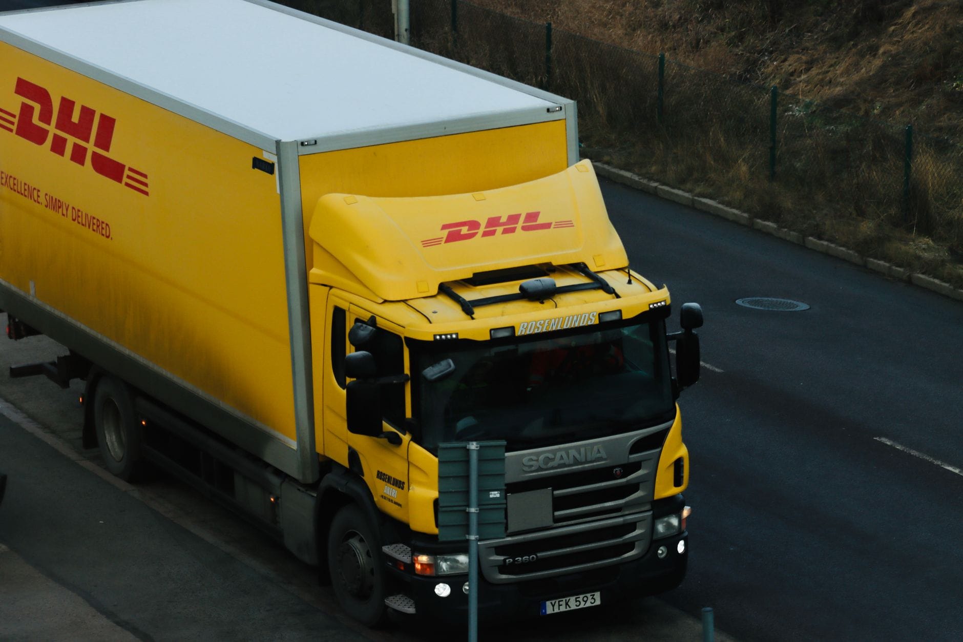 Żółta ciężarówka DHL jedzie miejską ulicą podczas realizacji dostawy