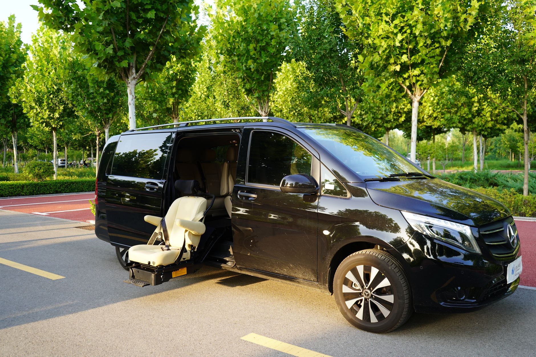 Czarny bus Mercedes z otwartymi drzwiami stoi w słonecznym, zielonym miejscu