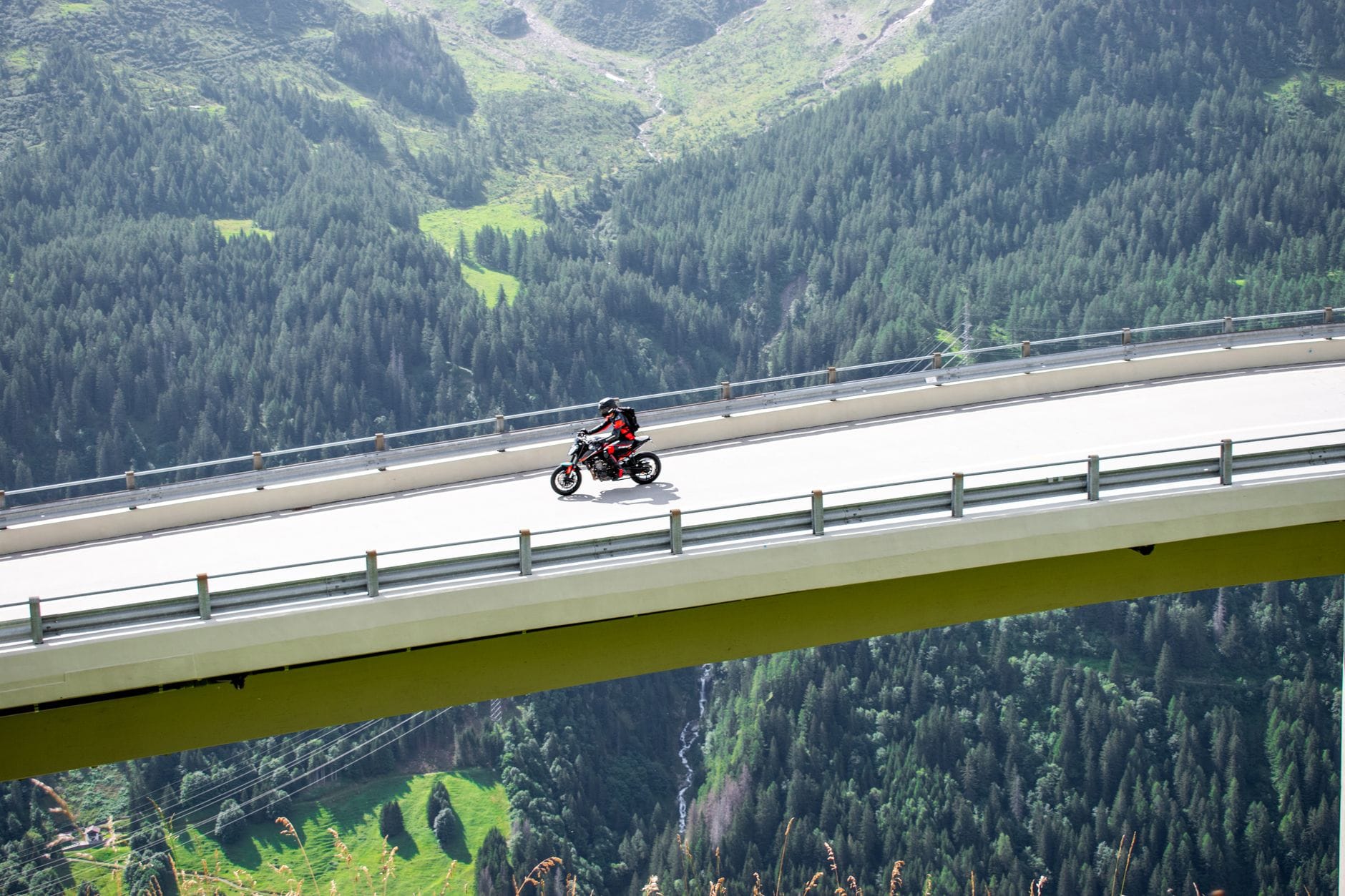Motocyklista na wiadukcie nad lasem w górskim krajobrazie