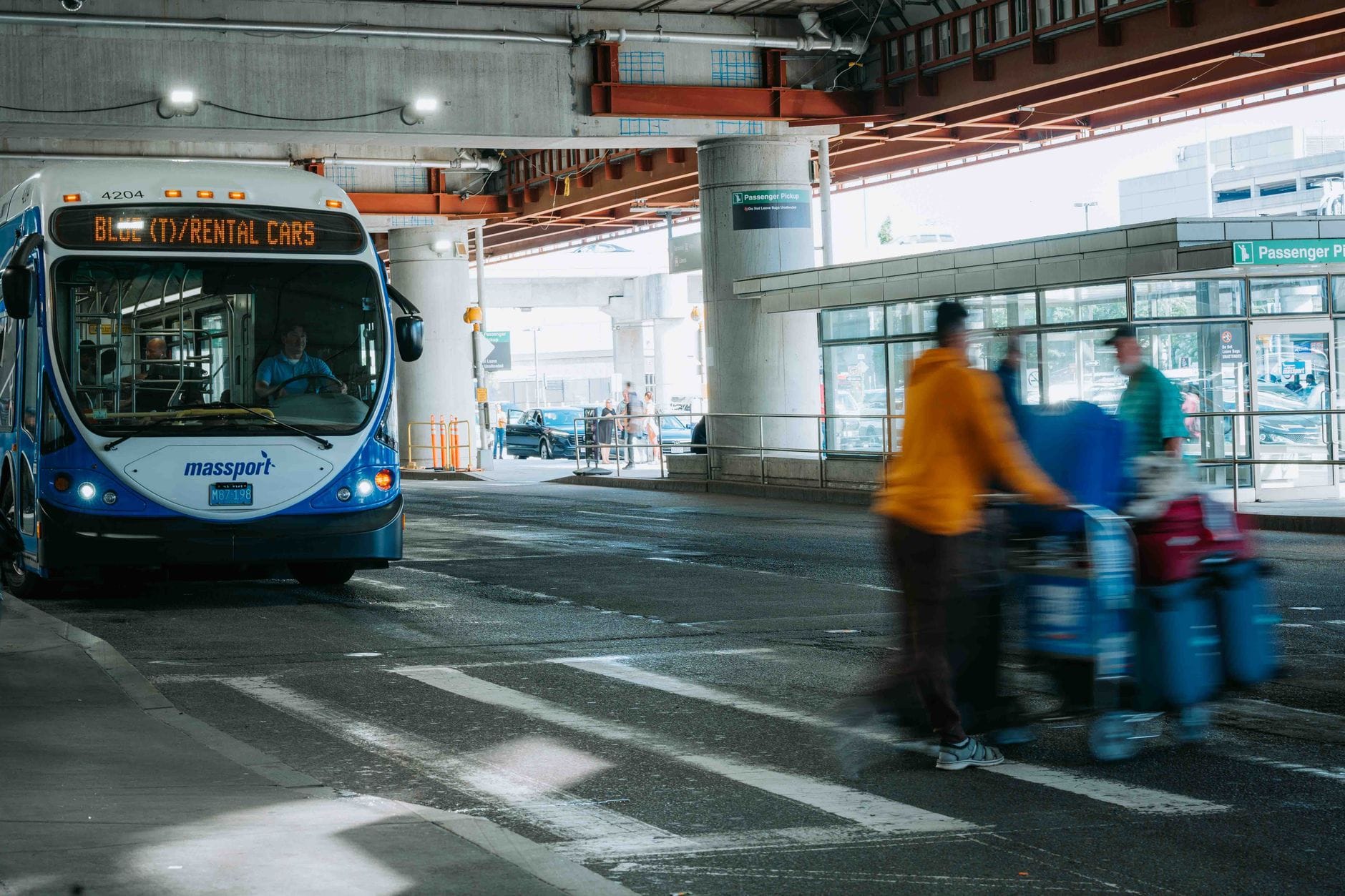 Podróżni z bagażem przy lotnisku, obok czeka bus wahadłowy