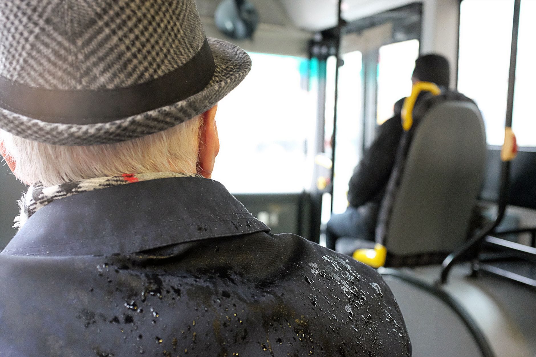 Starszy mężczyzna w kapeluszu siedzi w autobusie w deszczowy dzień